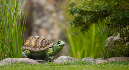 Decorative garden toy, ceramic turtle on stone, green juicy grass in the foreground.の写真素材