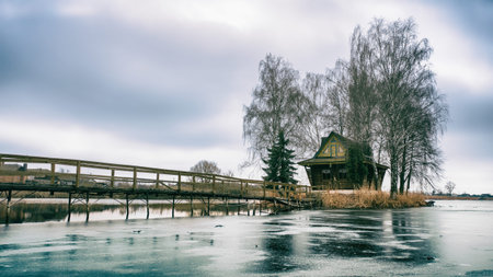 Morning landscape, wooden hunting lodge, on a small man-made island. A wooden platform is coming to...