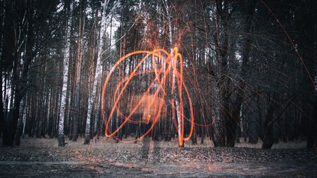A man makes sparks from steel wool, or cotton wool, in an autumn deciduous forest. Mystical background, soft focus.の写真素材