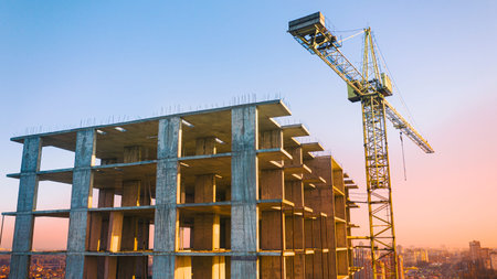 Multi-storey building, tower crane and construction site, top view. At sunset.