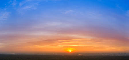 Dawn sky, sun rays paint the clouds in yellow and orange colors, on a background of blue skyの写真素材