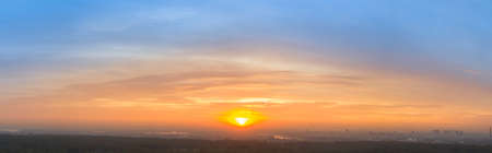 Dawn sky, sun rays paint the clouds in yellow and orange colors, on a background of blue skyの写真素材
