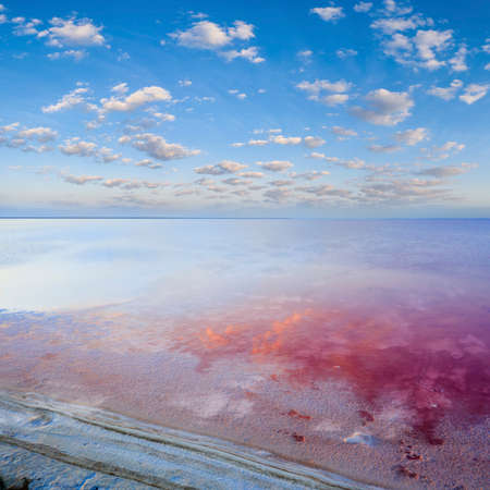 Sunset on Lake Lemuria. Red salt lies on the shore. Clouds are reflected in the water surface.の写真素材