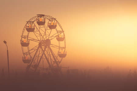 Ferris wheel in the park at dawn. Wonderful summer landscape. The sun's rays illuminate the morning mist.の写真素材