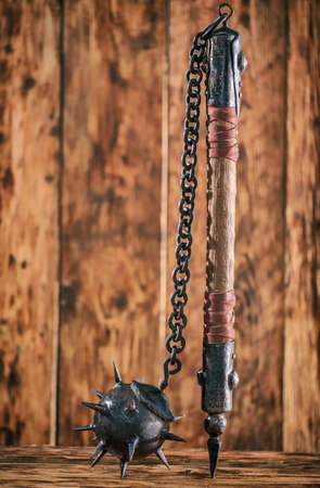 Ancient mace with wooden handle with metal tips, core and spikes, on wooden background.の写真素材