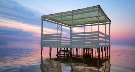 Bungalow for relaxation on the water, on a background of bright sunset. The orange sky is reflected in the clear sea water. Great place for tourism and recreation.の写真素材