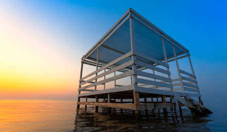 Bungalow for relaxation on the water, on a background of bright sunset. The orange sky is reflected in the clear sea water. Great place for tourism and recreation.の写真素材