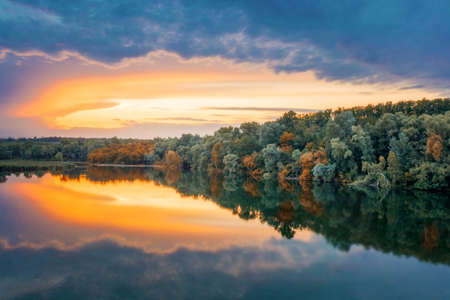 Bright orange-blue sky reflected in the calm clear water of the lake. Fresh summer morning. Picturesque landscape in the countryside.の写真素材