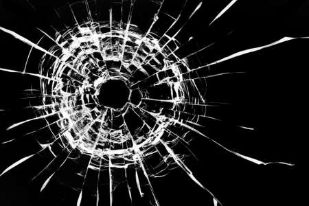 Cracks in the window. Bullet hole in the glass. Isolated on a black background.の写真素材