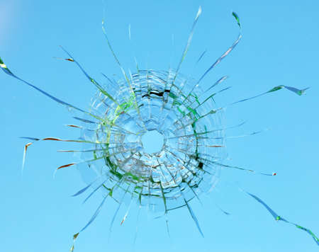 Cracks in the window glass on a background of sky.の写真素材