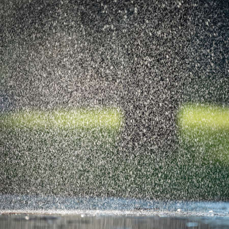 Raindrops fall on the asphalt and green grass.の写真素材