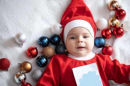 Toddler in a suit of Santa Claus with Christmas tree decorations.の写真素材