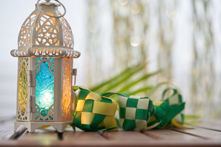 Ornamental Arabic lantern with burning candle glowing in dark and ribbon ketupatの写真素材