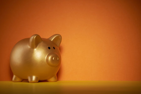 gold colored piggy bank against orange backgroundの写真素材