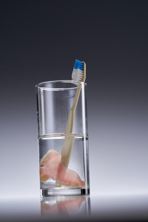 denture in a glass of water with toothbrush, Dental prosthesis care.の写真素材