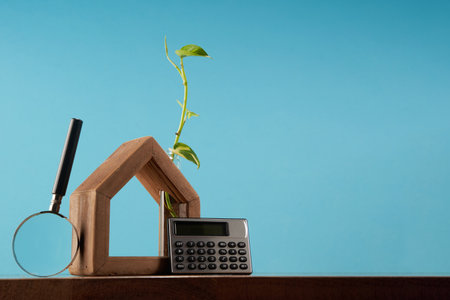 hand made wooden house  with money plant growth and calculator against blue backgroundの写真素材