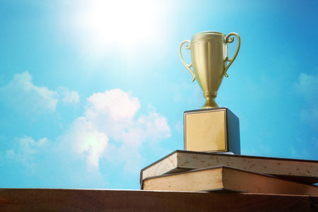 winning trophy on stack of book outdoor with light flareの写真素材