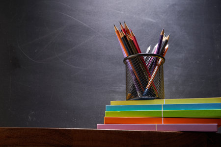 pencil holder on top stack of books against blackboardの写真素材