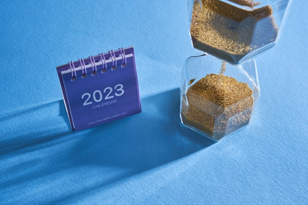 hourglass and 2023 desk calendar against blue background