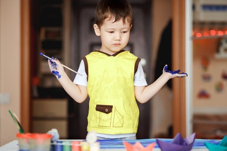 A little boy in a yellow T-shirt stained with paint after the painting does not know what to do. Little painter.の写真素材