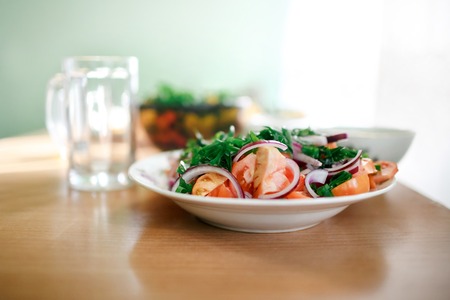 Minimalistic fresh mixed vegetable salad of tomatoes, onions and parsley. Empty glass mug in the background. Healthy food, vitamins in harsh living conditions, simple food, economy. Natural light, selective focus. Healthy breakfast, weight loss concept.の写真素材