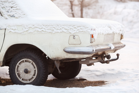 The rear of the car trunk covered with snow in winter, old broken white color at sunset. Recycling, metal processing, write-off of cars.の写真素材