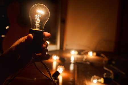 Incandescent light bulb, a warm light turned on in the dark, in the hands of a person. Garland of tungsten lamps. The light in the darkness, copy space.の写真素材