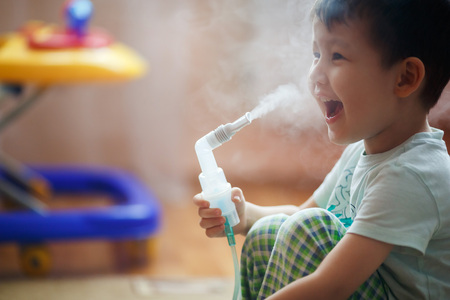 Little boy makes inhalation at home, taking medication to the bronchial tubes. Exhales steam through the tube.の写真素材