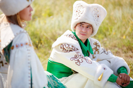A man on the grass in the traditional attire looks at his beloved woman