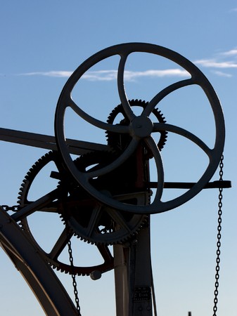 Silhouette of cogs, wheels and chains against a blue skyの写真素材