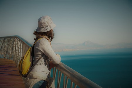 View of the bay of Alicante from the viewpoint with young woman leaning on a railing facing the sea on a sunny dayの写真素材