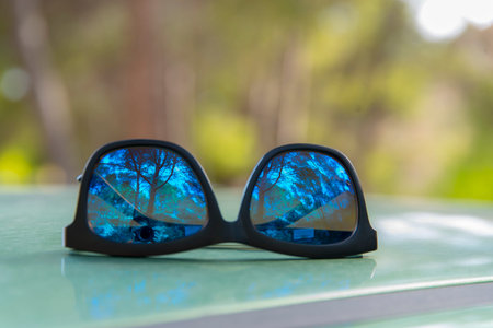 Sunglasses on the roof of a car Reflection of a forest outdoors in a lenses on a completely diffuse backgroundの写真素材