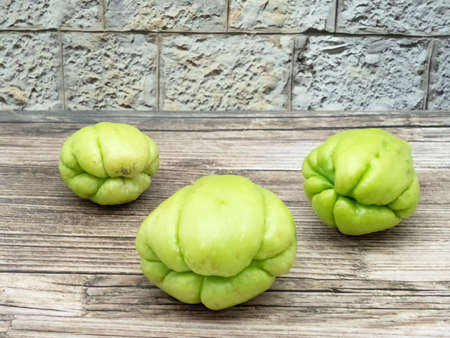Three fruits of chayote on wood in front of a wallの写真素材