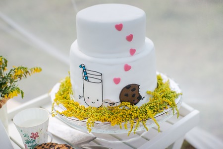 Funny wedding cake from mastic with a mug of milk and cookies. White wedding cake with flowers.の写真素材