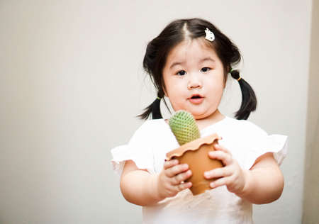 2 years old girl is holding a small pot of cactus