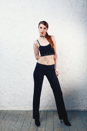 Redhead model woman standing and posing on white wall in sexy lace top and black jeans with naked stomachの写真素材