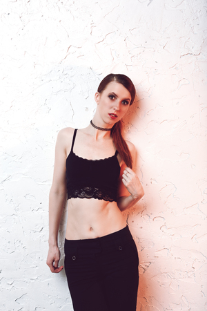 Redhead model woman standing and posing on white wall in sexy lace top and black jeans with naked stomachの写真素材