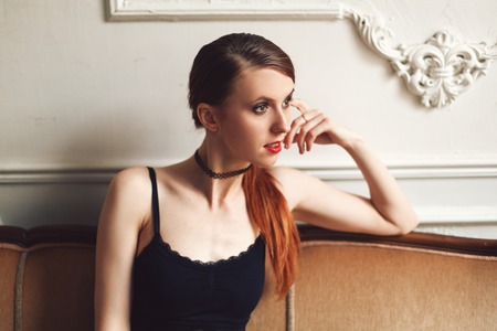 Attractive young woman sitting and posing on sofa in sexy lace top and black jeans with naked stomachの写真素材