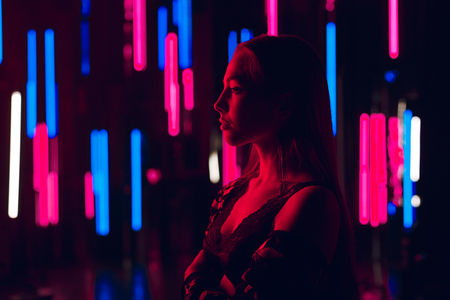 Portrait of beautiful young woman standing against a wall of neon tubes in sexy lingerie and fully openned kimono with naked shouldersの写真素材