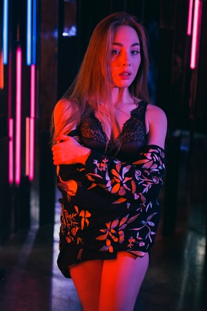 Sexy young woman standing and posing in sexy lingerie in a room of neon lightsの写真素材
