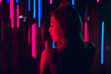 Sensual young woman staying topless showing her beautiful back against a wall of neon lightの写真素材