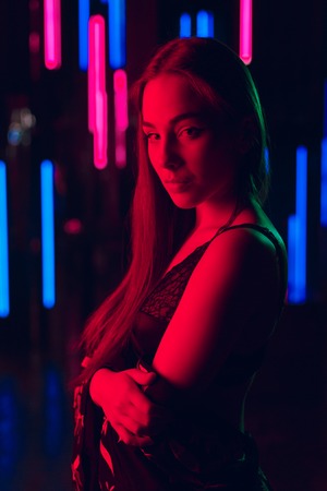 Portrait of attractive young woman standing against a wall of neon tubes in sexy lingerie and fully openned kimonoの写真素材