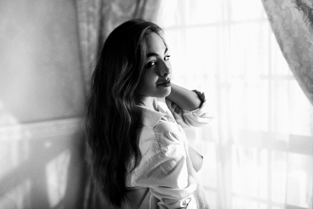 Beautiful girl with long hairs in unbuttoned man's shirt teasingの写真素材