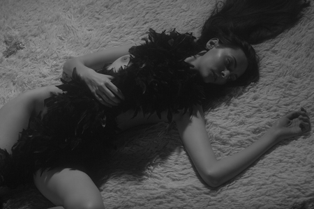 Sexy young woman with long black hair lying naked in feather scarf on a bed enjoing a momen and getting ready to Helloween party.の写真素材
