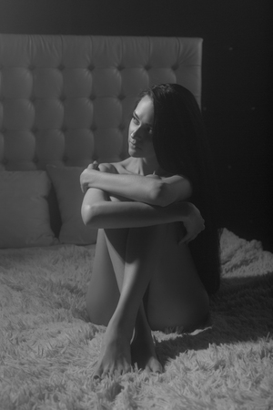 Sexy young woman in a image of witch with a very long black hair sitting naked on her bed and looking on light.の写真素材