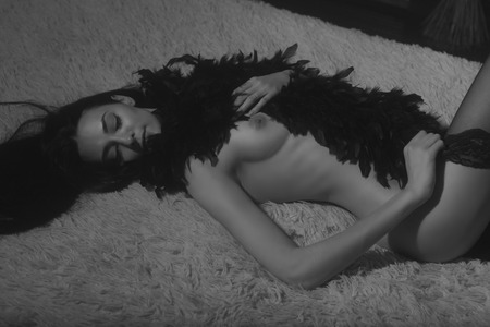 Beautiful young woman lying naked in feather scarf on a bed enjoing a momen and getting ready to Helloween party.の写真素材