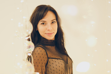 Beautiful young woman in cocktail dress staying smiling over lights background with shallow depth of fieldの写真素材