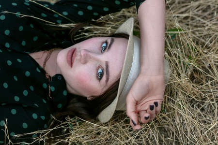 A young woman in a straw hat lies on a haystack. Female portrait in field in countryside.の写真素材