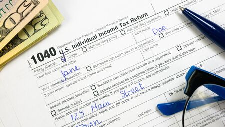 U.S. Dollar Banknotes on Filled 1040 Tax Form. Blue Pen on Document. Individual Income Tax Return. Filing Taxes Documentの写真素材