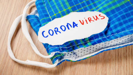 Face mask and coronavirus inscription on table background. 2019-nCoV or COVID-19 concept.